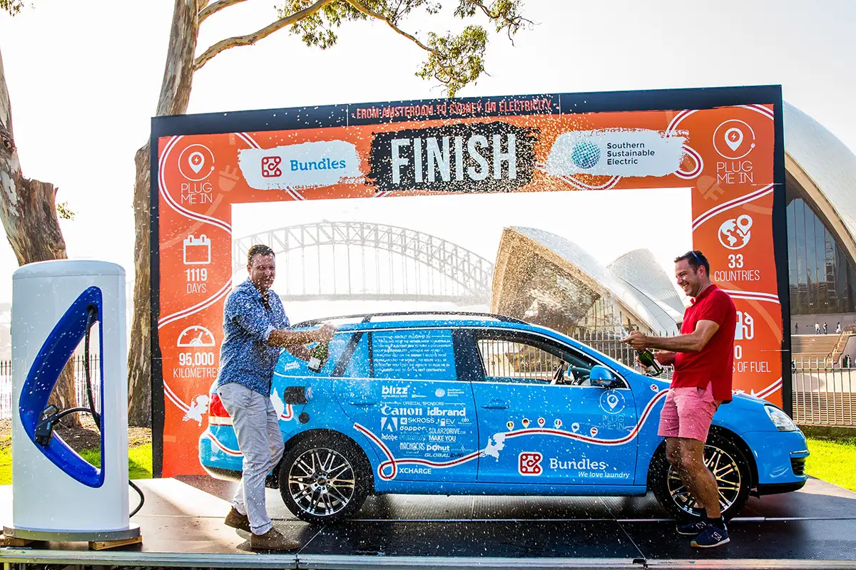 Wiebe Wakker staat op het podium met zijn elektrische auto Blue Bandit en viert de voltooiing van zijn Plug Me In-project in Sydney, Australië.