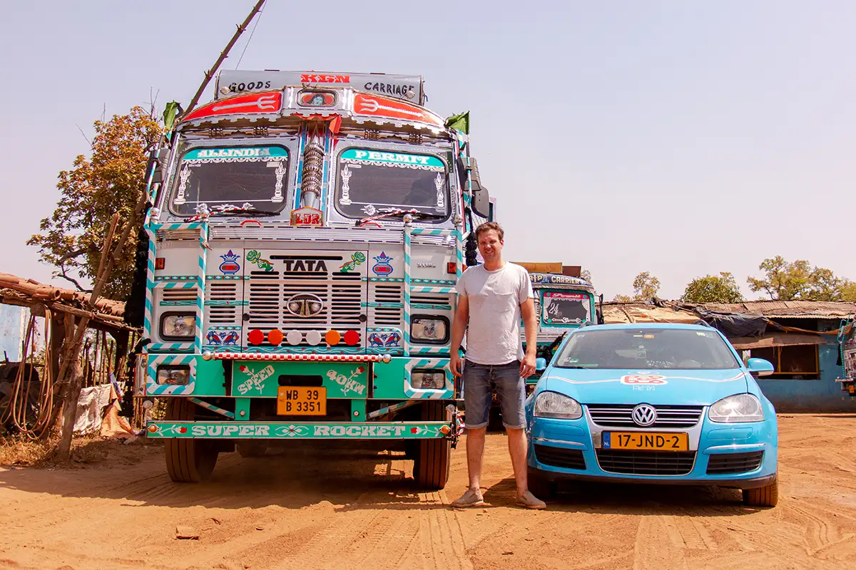 Wiebe Wakker en zijn elektrische auto staan naast een grote vrachtwagen op het Indiase platteland.