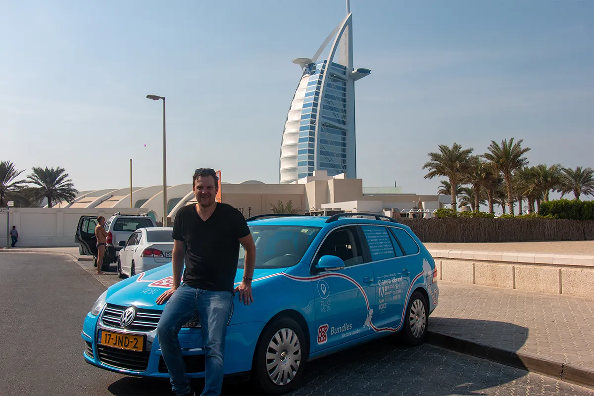 Wiebe Wakker sitting on the bonnet of his electric car, standing in front of Burj Al Arab in Dubai, UAE.