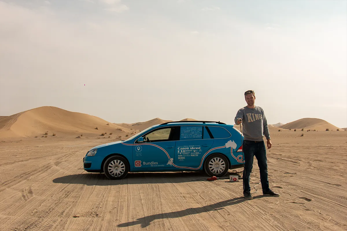 Wiebe Wakker met een stekker in zijn hand, voor zijn auto in de Varzaneh-woestijn, Iran.